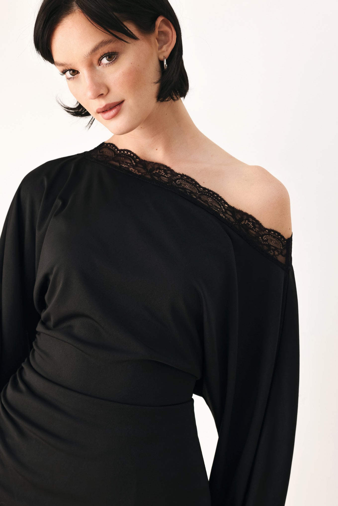 A model wearing a black asymmetrical off-the-shoulder top with black lace trim along the neckline, cuffs, and hem | FREEMARKET