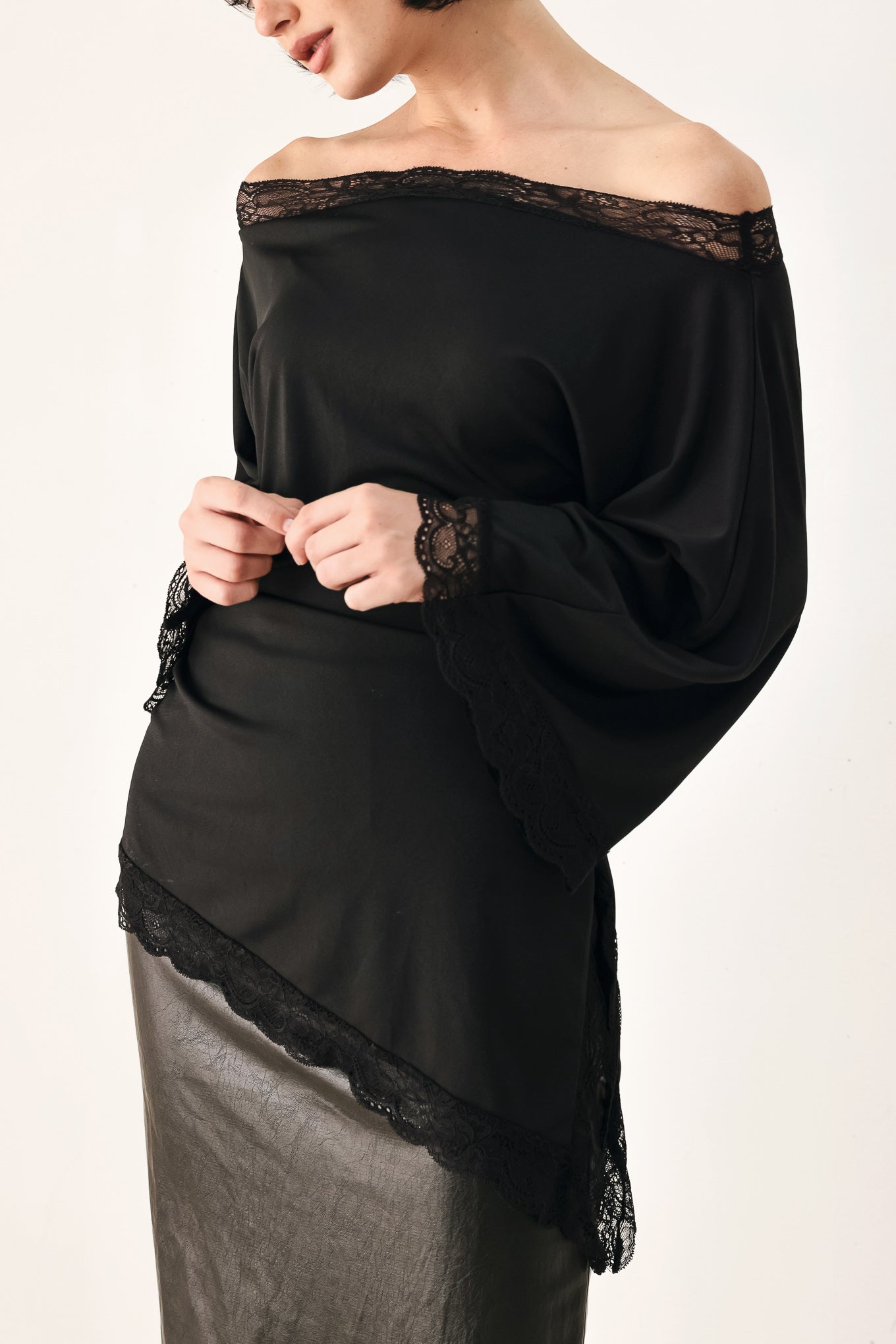 A model wearing a black asymmetrical off-the-shoulder top with black lace trim along the neckline, cuffs, and hem | FREEMARKET