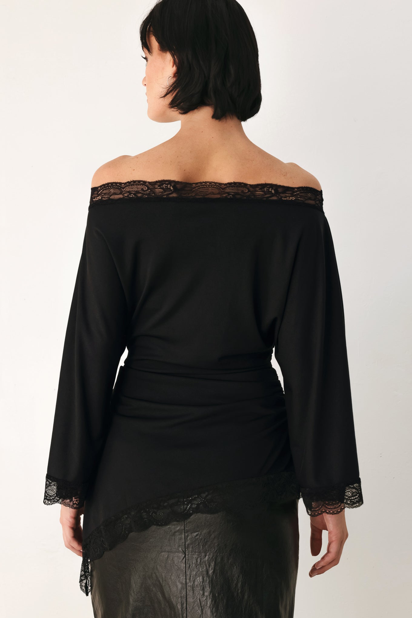 A model wearing a black asymmetrical off-the-shoulder top with black lace trim along the neckline, cuffs, and hem | FREEMARKET