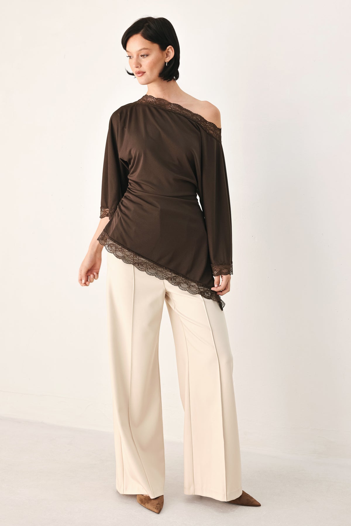 A model wearing a dark brown asymmetrical off-the-shoulder top with brown lace trim along the neckline, cuffs, and hem | FREEMARKET