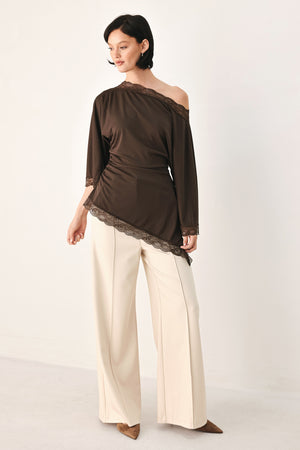 A model wearing a dark brown asymmetrical off-the-shoulder top with brown lace trim along the neckline, cuffs, and hem | FREEMARKET