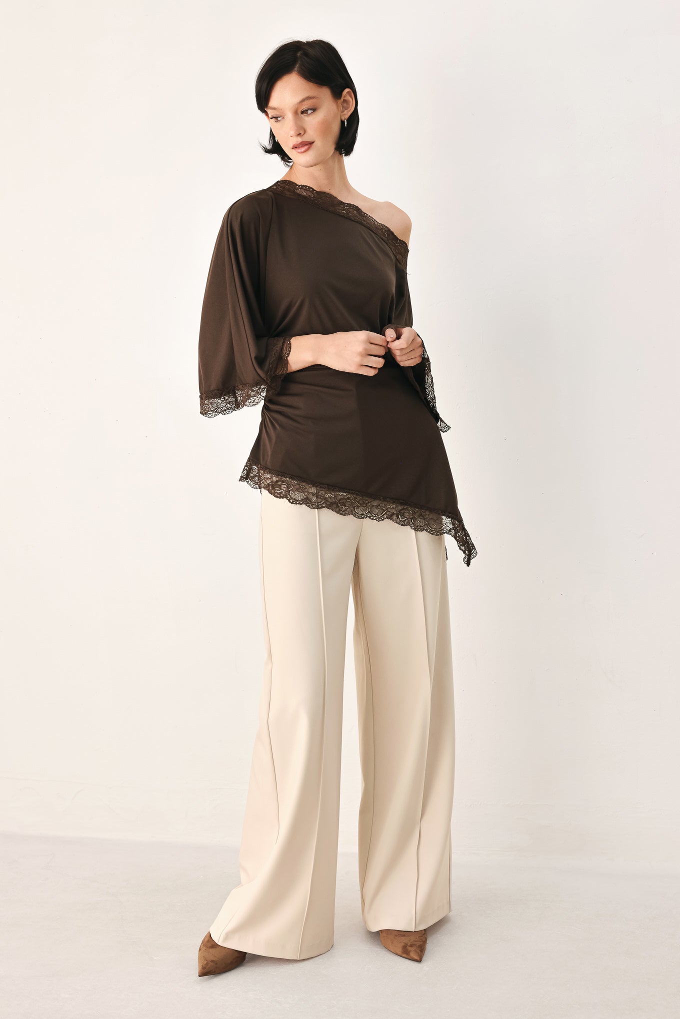 A model wearing a dark brown asymmetrical off-the-shoulder top with brown lace trim along the neckline, cuffs, and hem | FREEMARKET