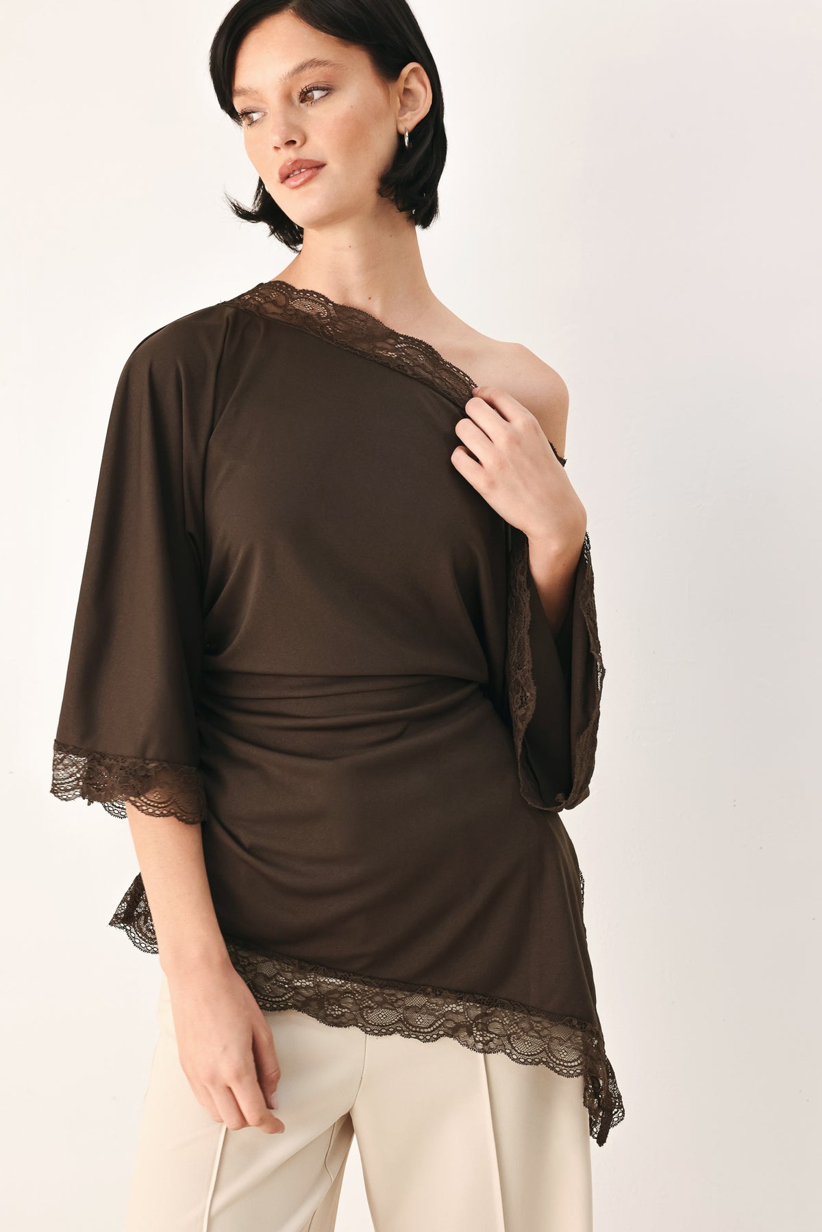 A model wearing a dark brown asymmetrical off-the-shoulder top with brown lace trim along the neckline, cuffs, and hem | FREEMARKET