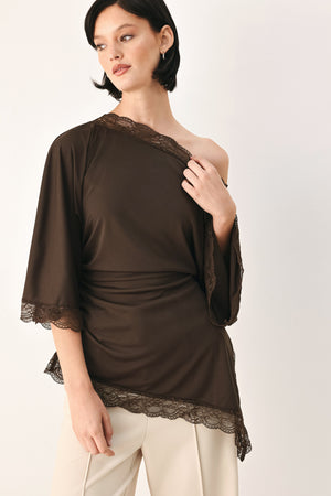 A model wearing a dark brown asymmetrical off-the-shoulder top with brown lace trim along the neckline, cuffs, and hem | FREEMARKET