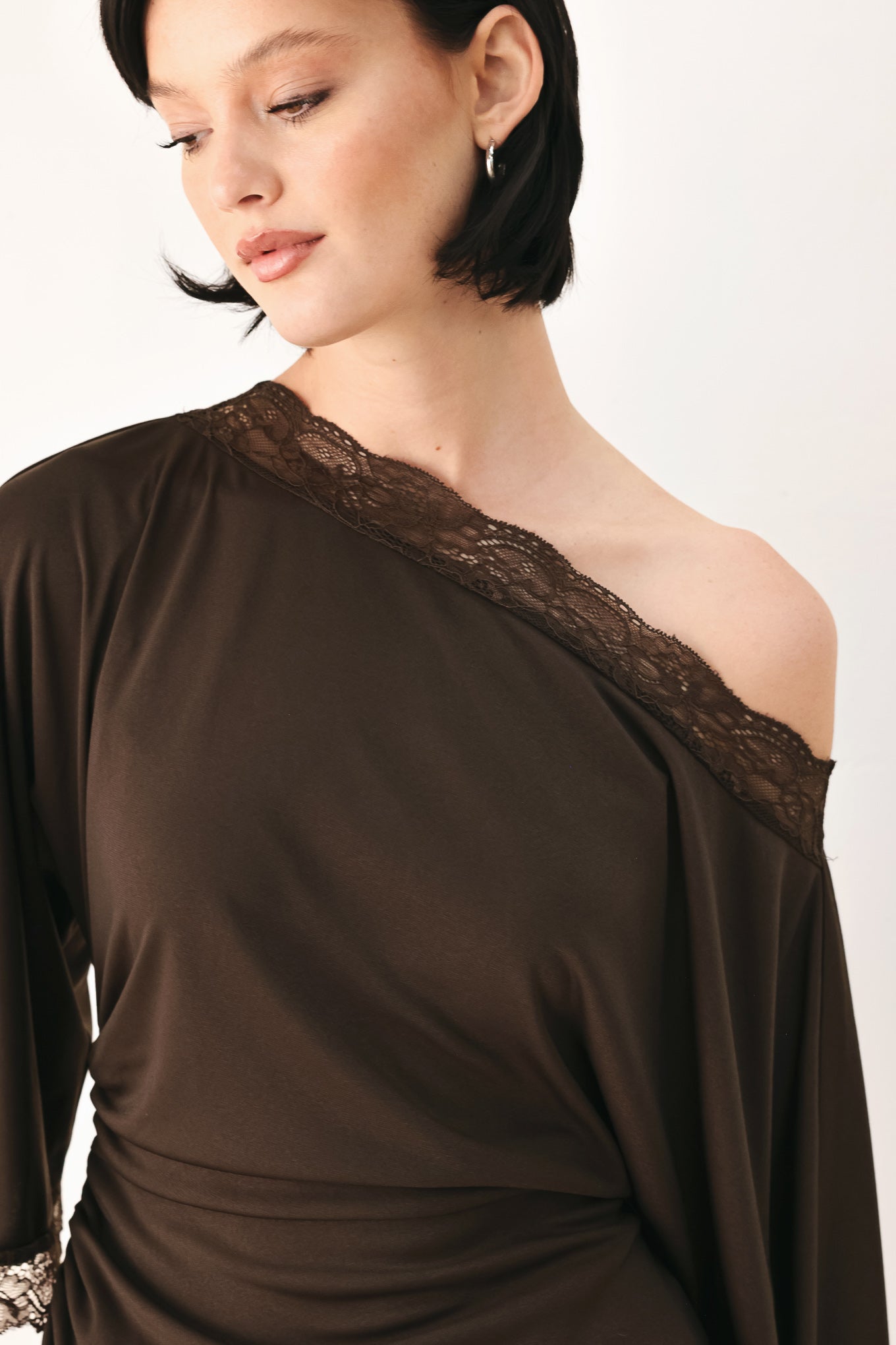 A model wearing a dark brown asymmetrical off-the-shoulder top with brown lace trim along the neckline, cuffs, and hem | FREEMARKET