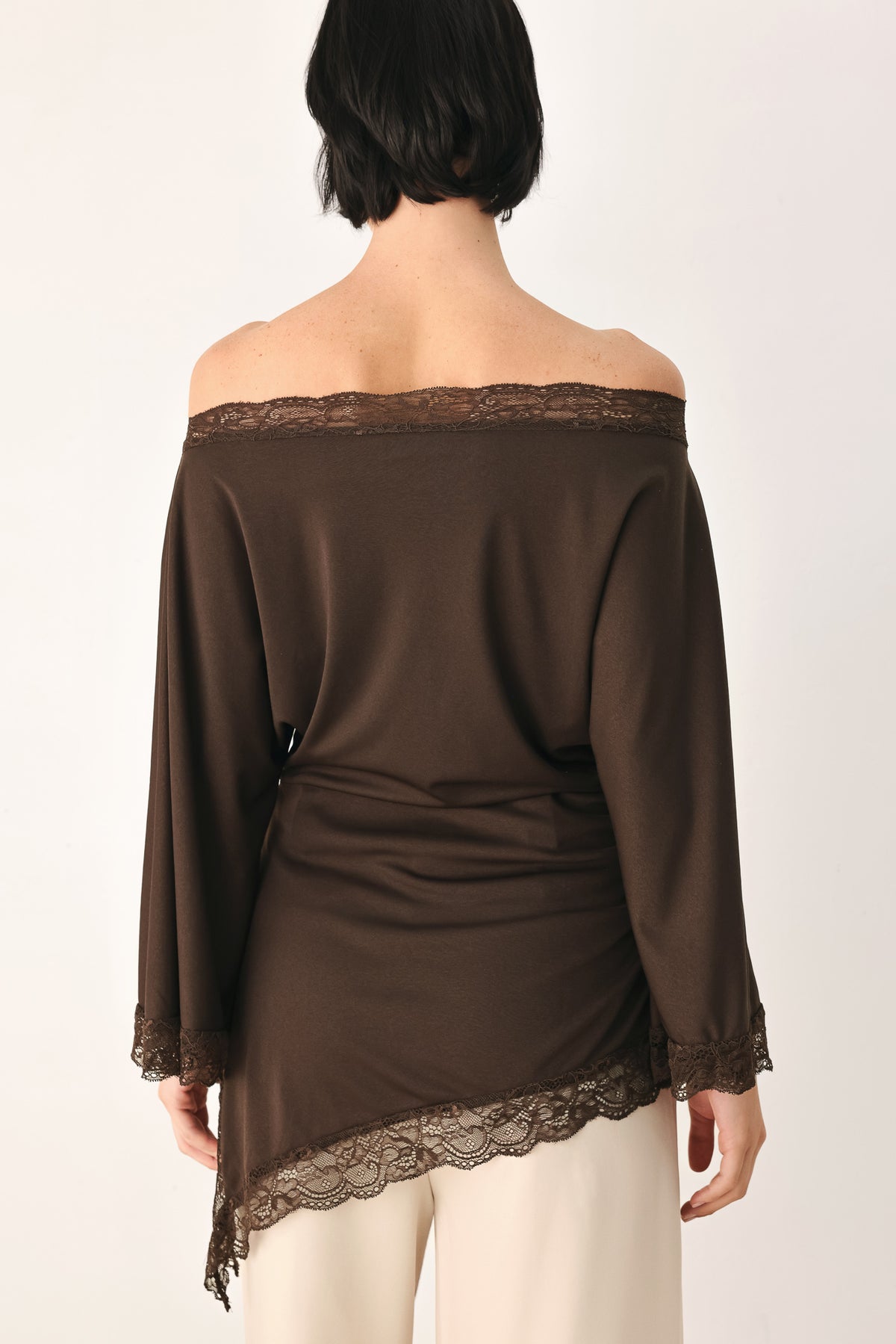 A model wearing a dark brown asymmetrical off-the-shoulder top with brown lace trim along the neckline, cuffs, and hem | FREEMARKET