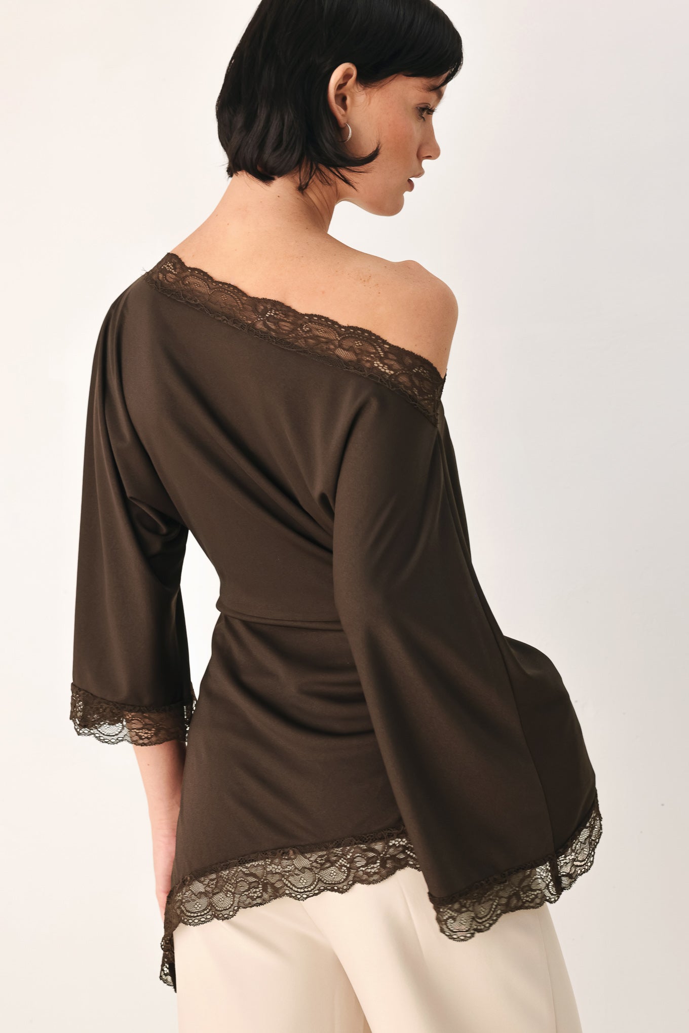 A model wearing a dark brown asymmetrical off-the-shoulder top with brown lace trim along the neckline, cuffs, and hem | FREEMARKET