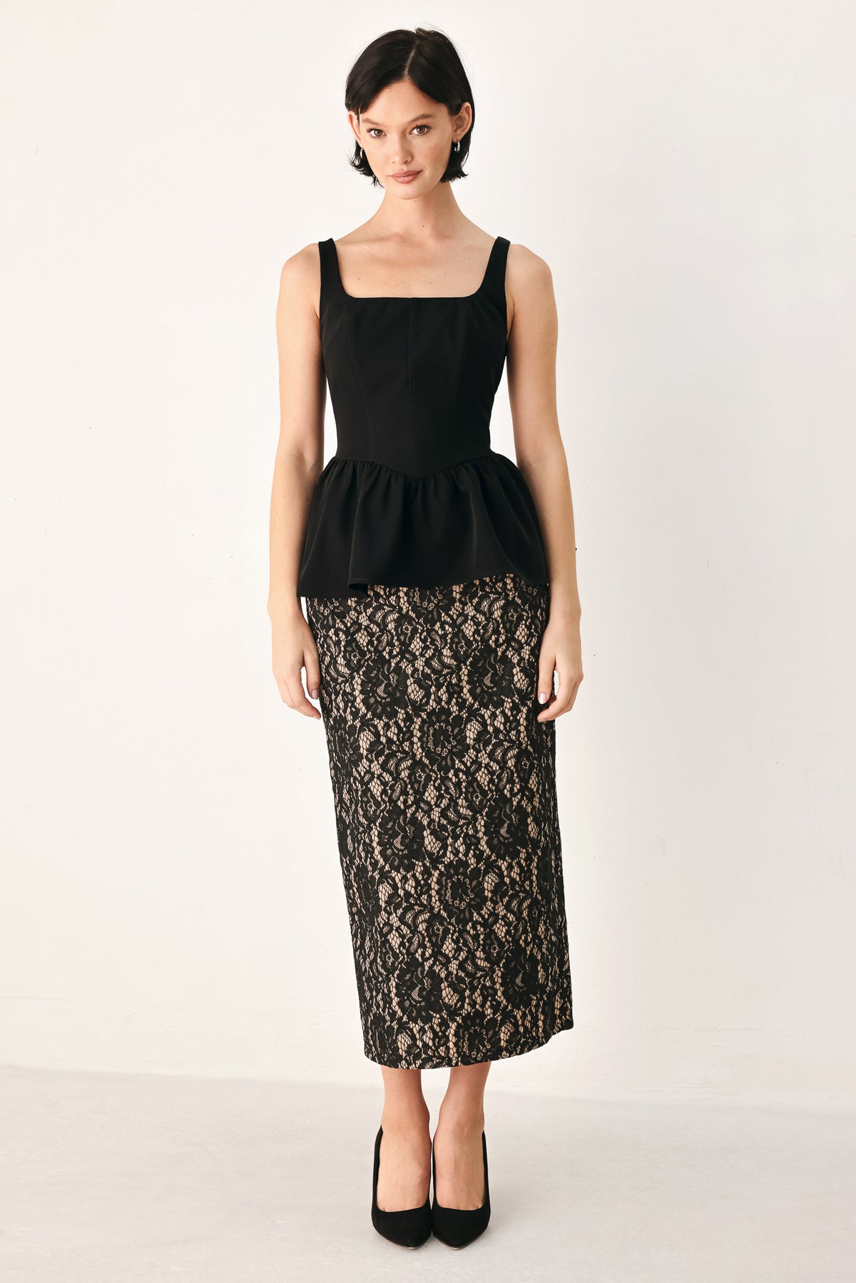 A woman wearing a black sleeveless peplum top with a square neckline and a flared ruffled waist | FREEMARKET