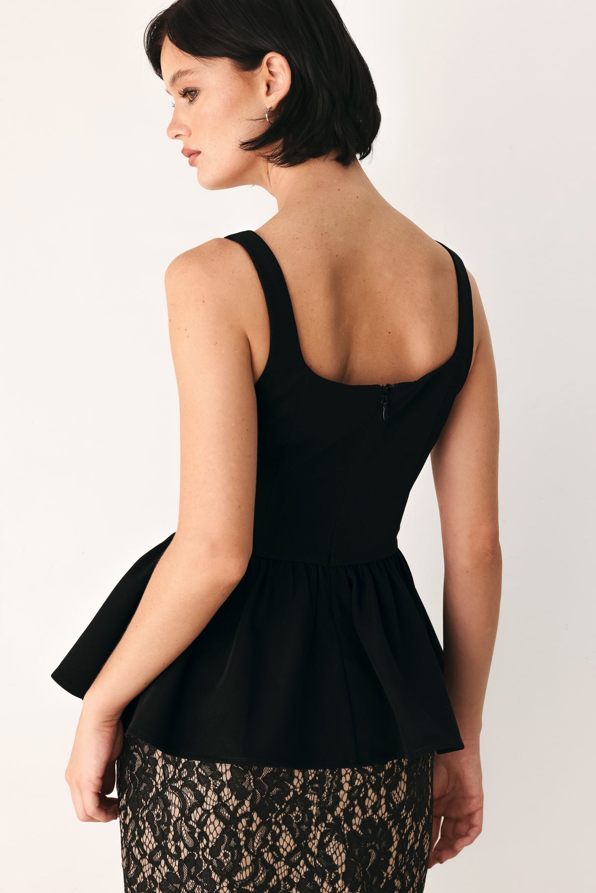 A woman wearing a black sleeveless peplum top with a square neckline and a flared ruffled waist | FREEMARKET