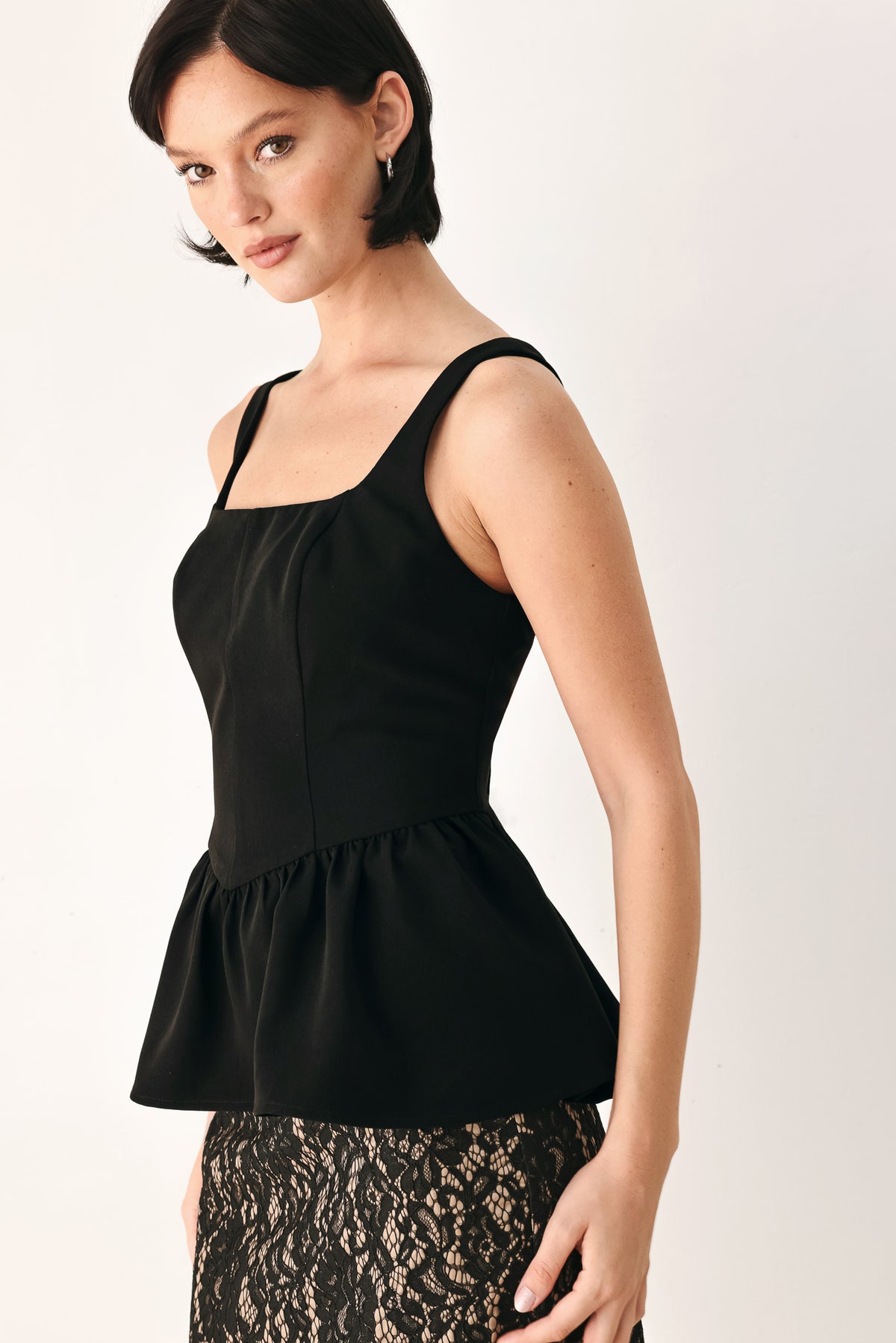 A woman wearing a black sleeveless peplum top with a square neckline and a flared ruffled waist | FREEMARKET