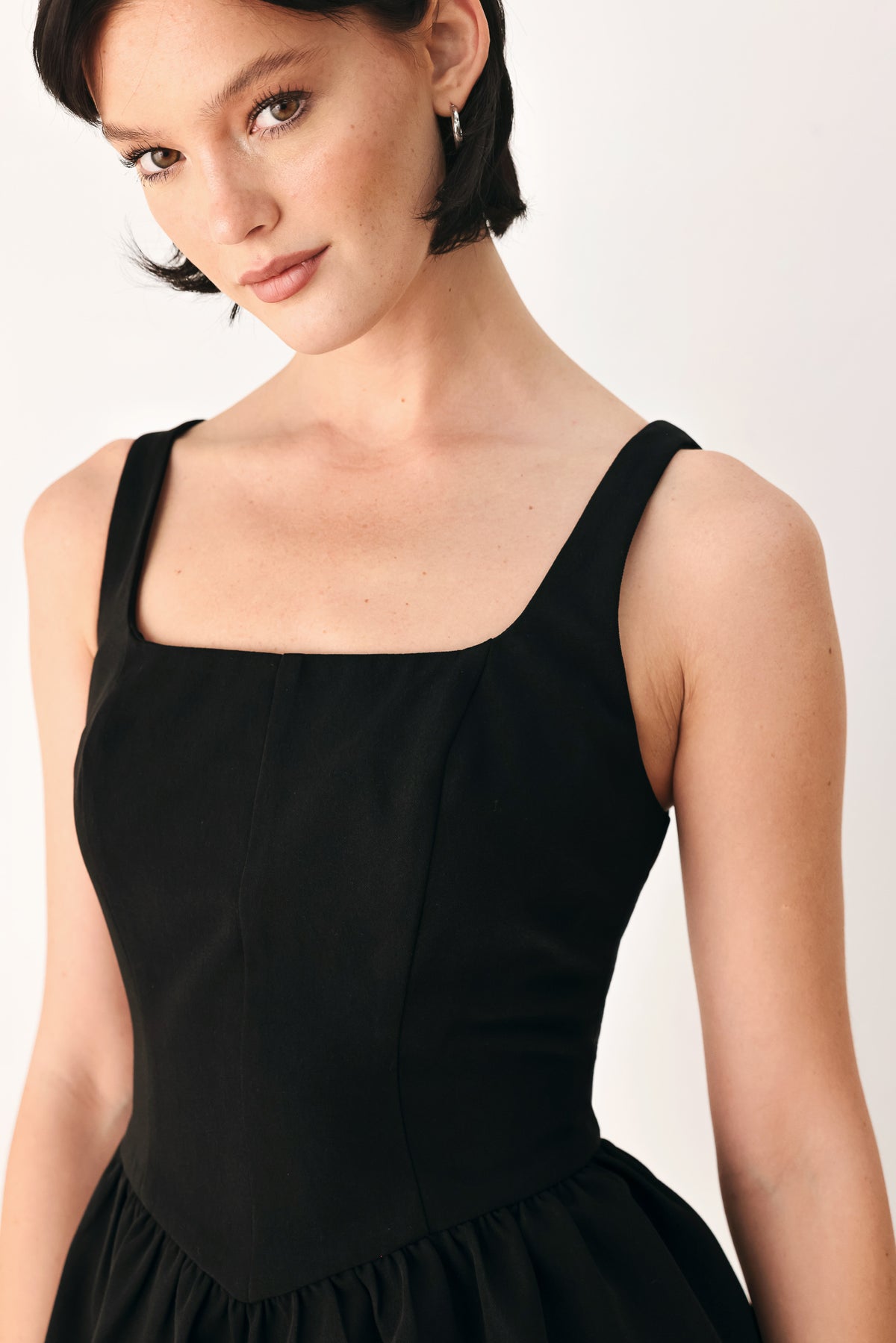 A woman wearing a black sleeveless peplum top with a square neckline and a flared ruffled waist | FREEMARKET