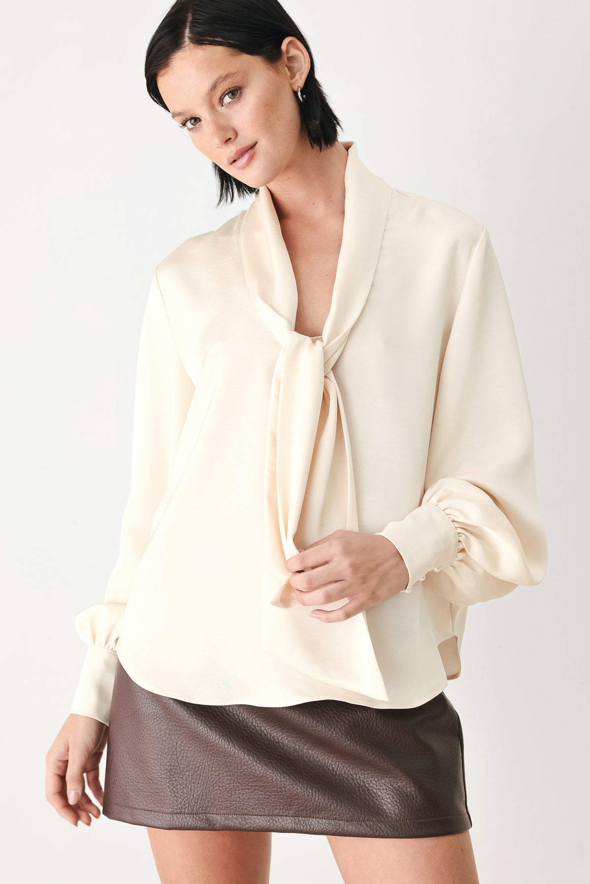 A woman wearing a cream-colored long-sleeve blouse with a tie-neck detail | FREEMARKET