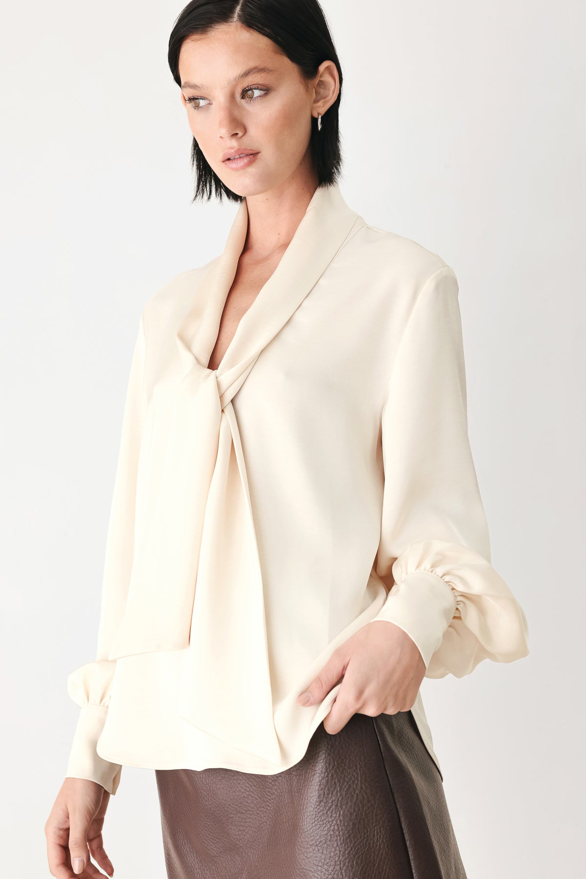 A woman wearing a cream-colored long-sleeve blouse with a tie-neck detail | FREEMARKET