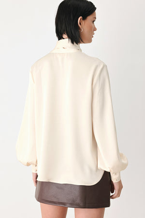 A woman wearing a cream-colored long-sleeve blouse with a tie-neck detail | FREEMARKET
