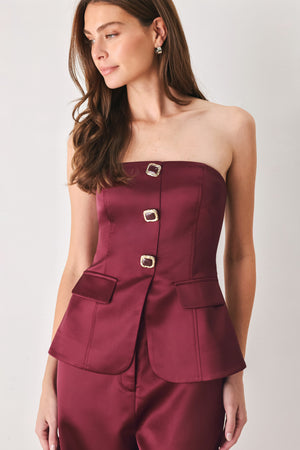 Woman wearing a burgundy strapless satin-like top with buttons along the front and two faux pockets | FREEMARKET