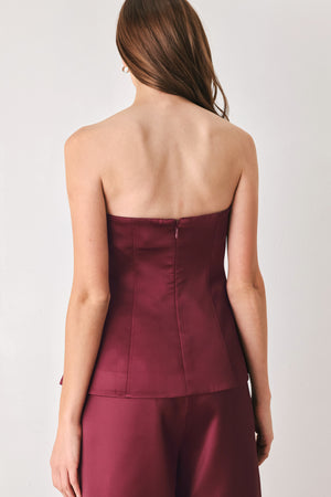 Woman wearing a burgundy strapless satin-like top with buttons along the front and two faux pockets | FREEMARKET