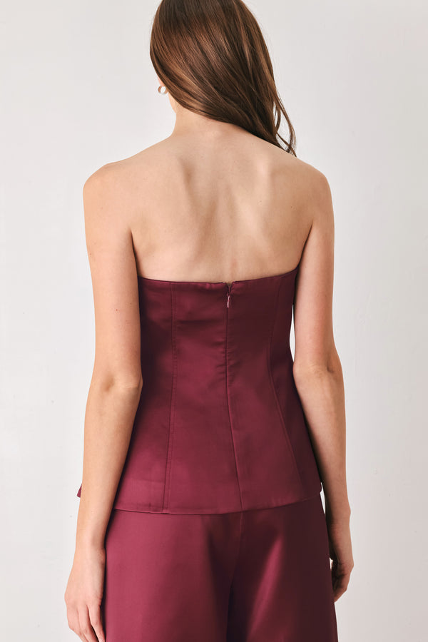 Woman wearing a burgundy strapless satin-like top with buttons along the front and two faux pockets | FREEMARKET
