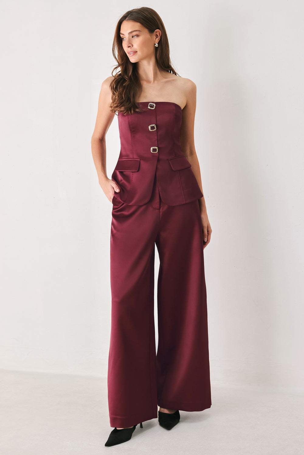 Woman wearing a burgundy strapless satin-like top with buttons along the front and two faux pockets | FREEMARKET