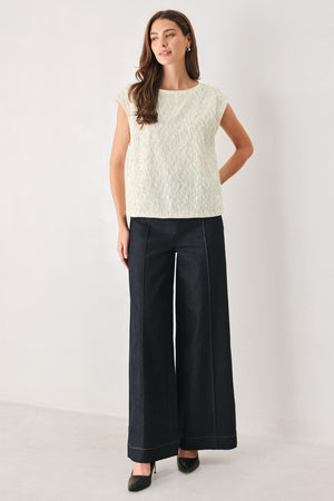 Woman wearing an off white cap sleeve. boat neck mid length top with sequin and light feather texture | FREEMARKET