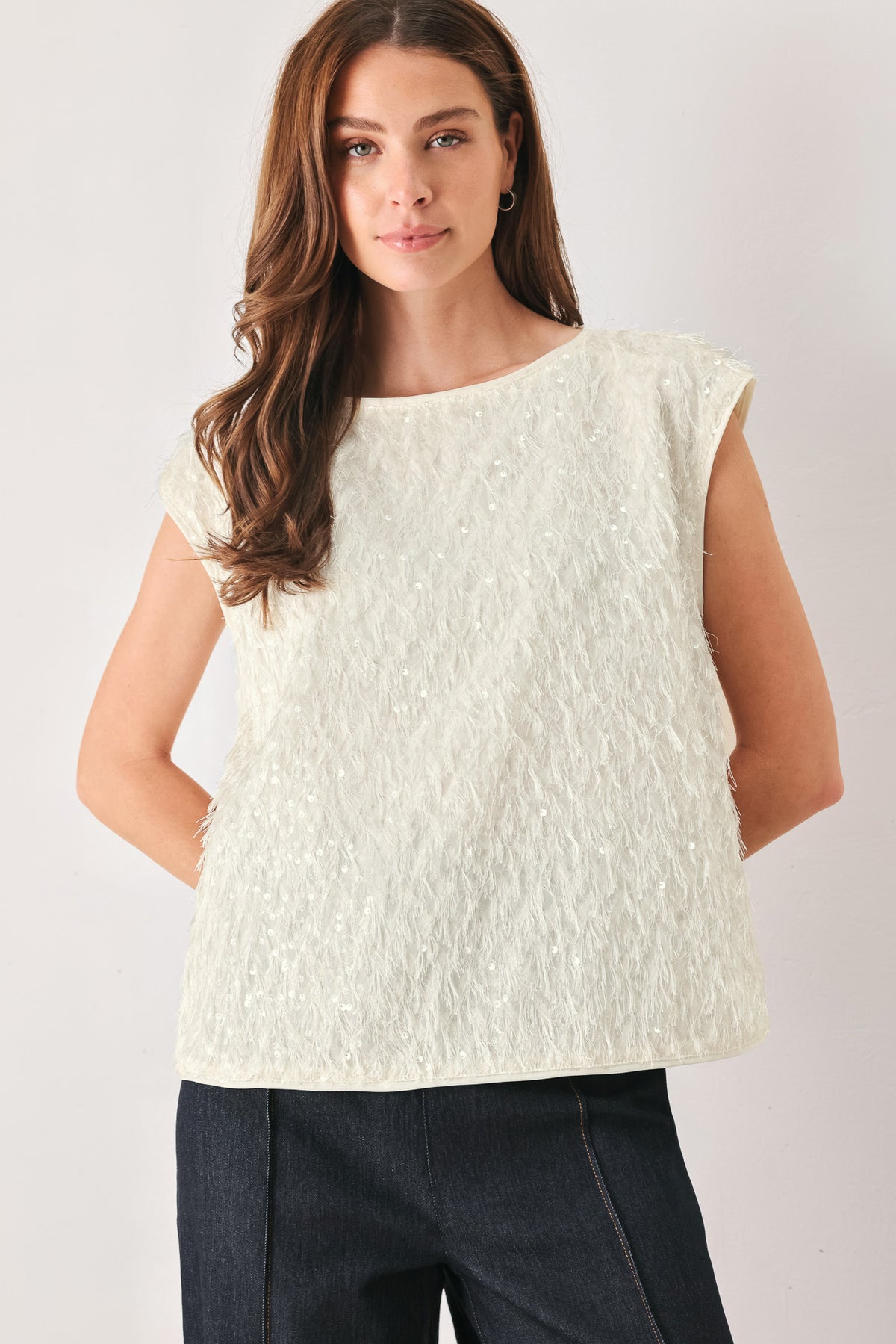 Woman wearing an off white cap sleeve. boat neck mid length top with sequin and light feather texture | FREEMARKET