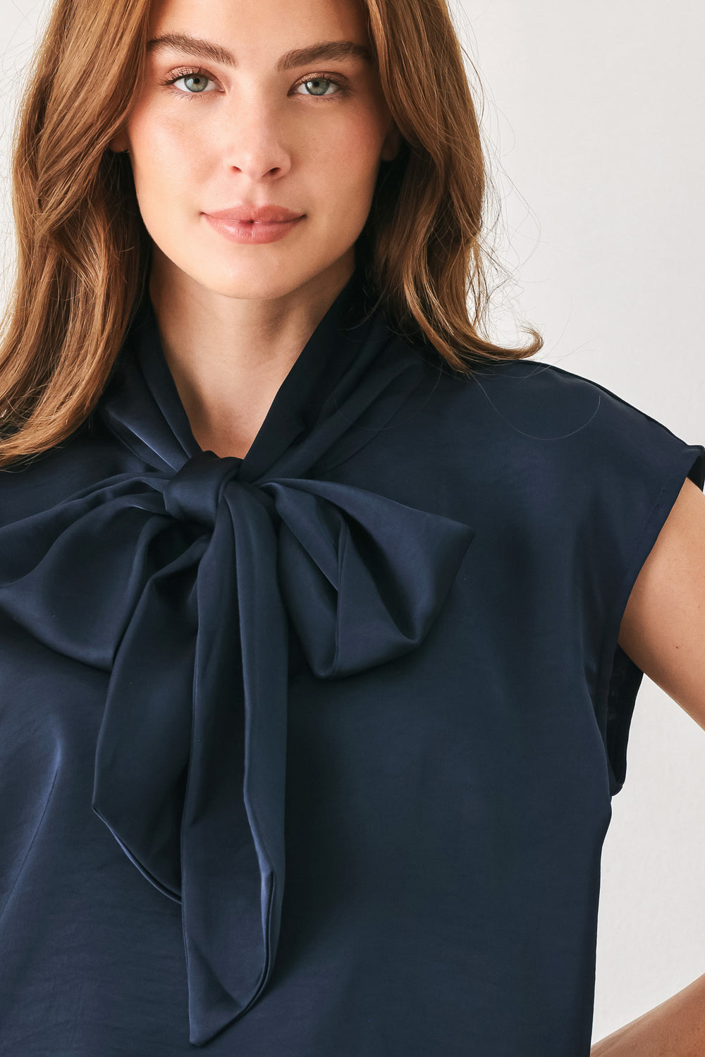 Woman wearing a navy blue cap sleeve satin top with a bow along the neck | FREEMARKET