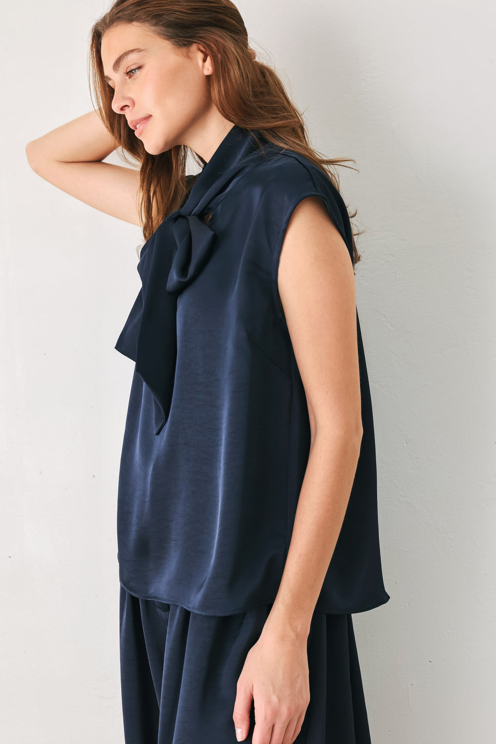 Woman wearing a navy blue cap sleeve satin top with a bow along the neck | FREEMARKET