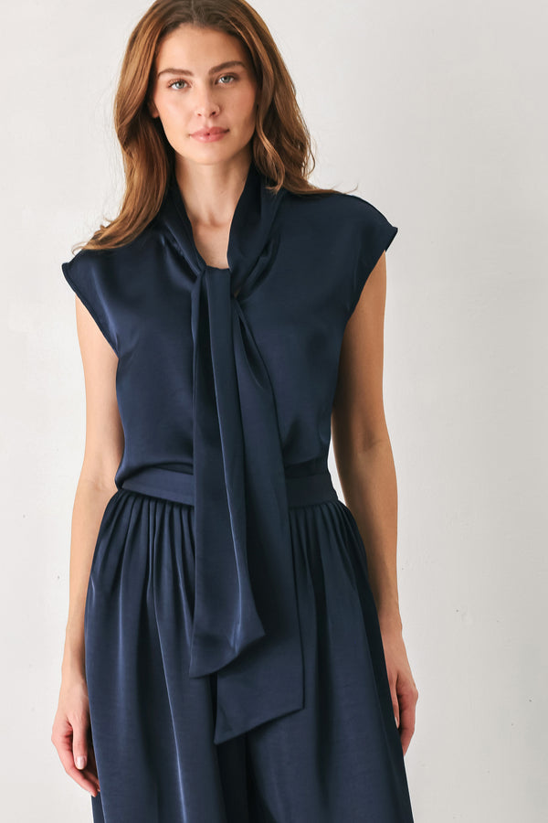 Woman wearing a navy blue cap sleeve satin top with a bow along the neck | FREEMARKET