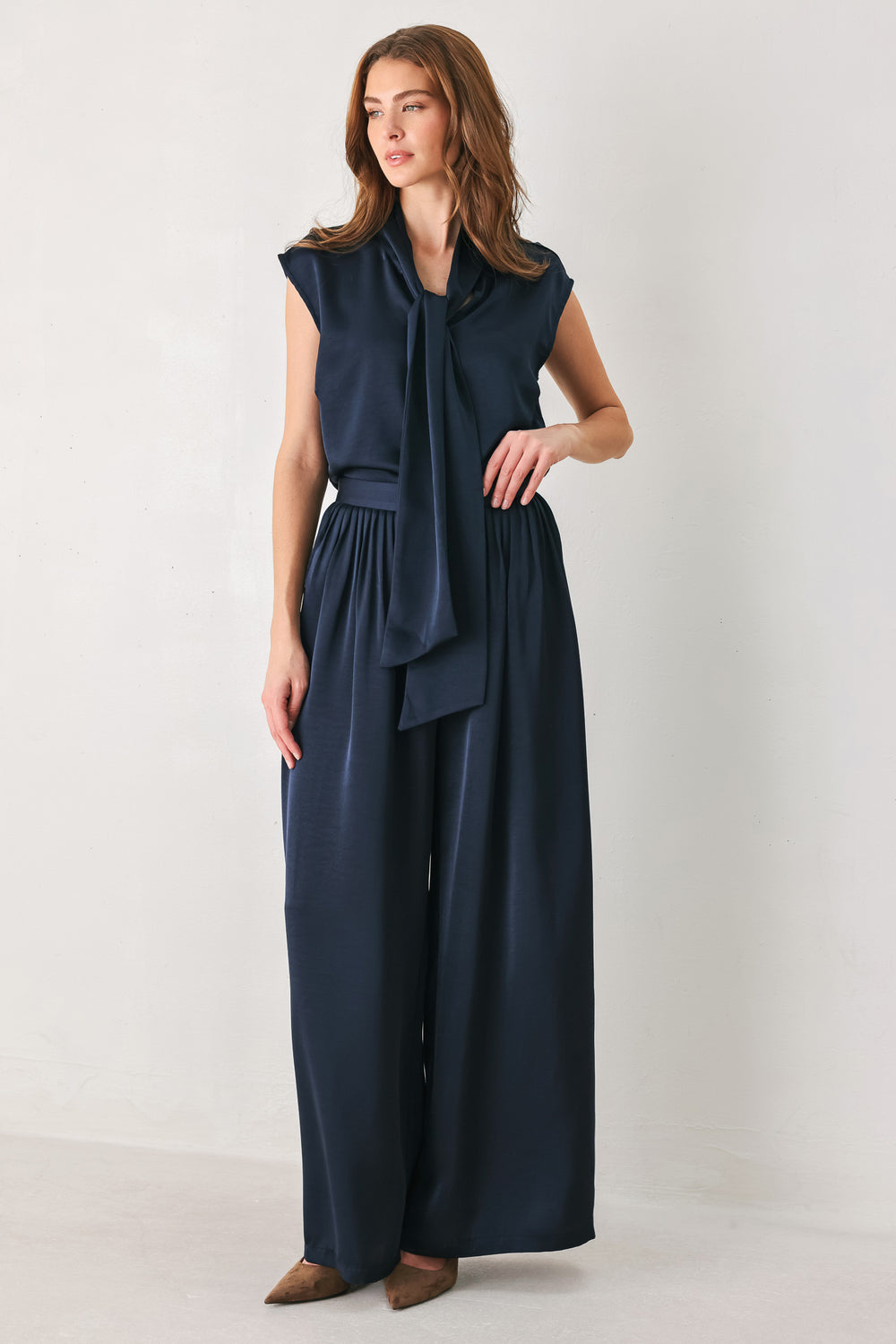 Woman wearing a navy blue cap sleeve satin top with a bow along the neck | FREEMARKET