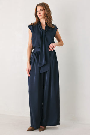 Woman wearing a navy blue cap sleeve satin top with a bow along the neck | FREEMARKET