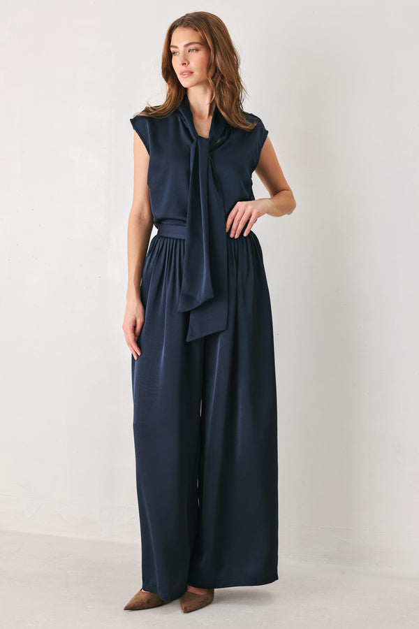Woman wearing a navy blue cap sleeve satin top with a bow along the neck | FREEMARKET