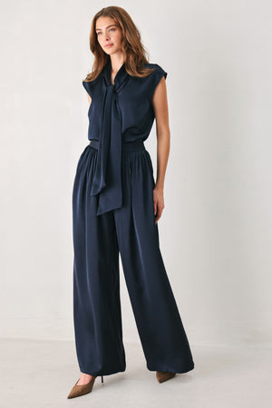 Woman wearing a navy blue cap sleeve satin top with a bow along the neck | FREEMARKET