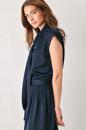 Woman wearing a navy blue cap sleeve satin top with a bow along the neck | FREEMARKET