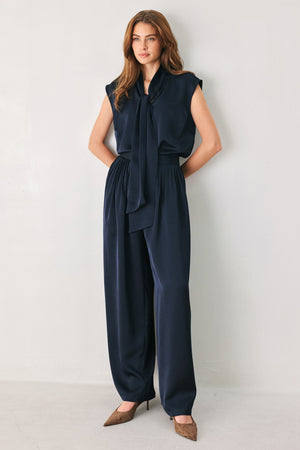 Woman wearing a navy blue cap sleeve satin top with a bow along the neck | FREEMARKET