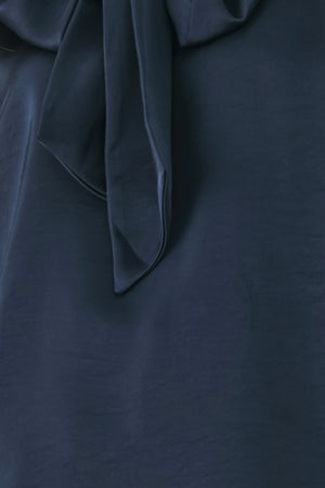Woman wearing a navy blue cap sleeve satin top with a bow along the neck | FREEMARKET