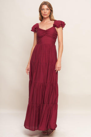 A solid woven maxi dress featuring cami top with layered sleeve, cinched front bodice, tiered skirt and smocked back bodice.