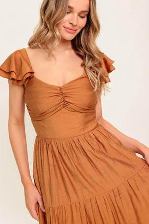 A solid woven maxi dress featuring cami top with layered sleeve, cinched front bodice, tiered skirt and smocked back bodice.