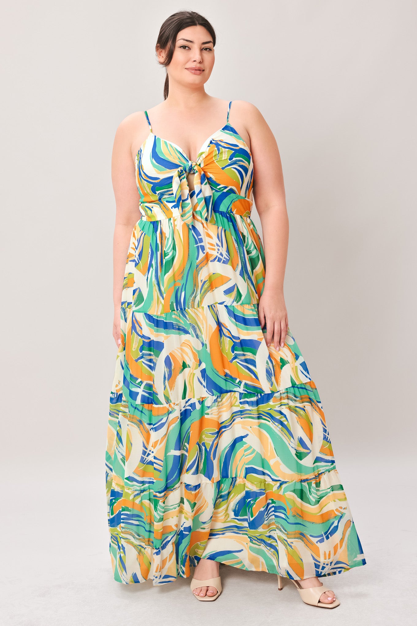 Woman wearing a colorful patterned maxi dress featuring cami bodice with front tie and cut out detail, tiered skirt and smocked back bodice on a plain background | Curve | Flying Tomato