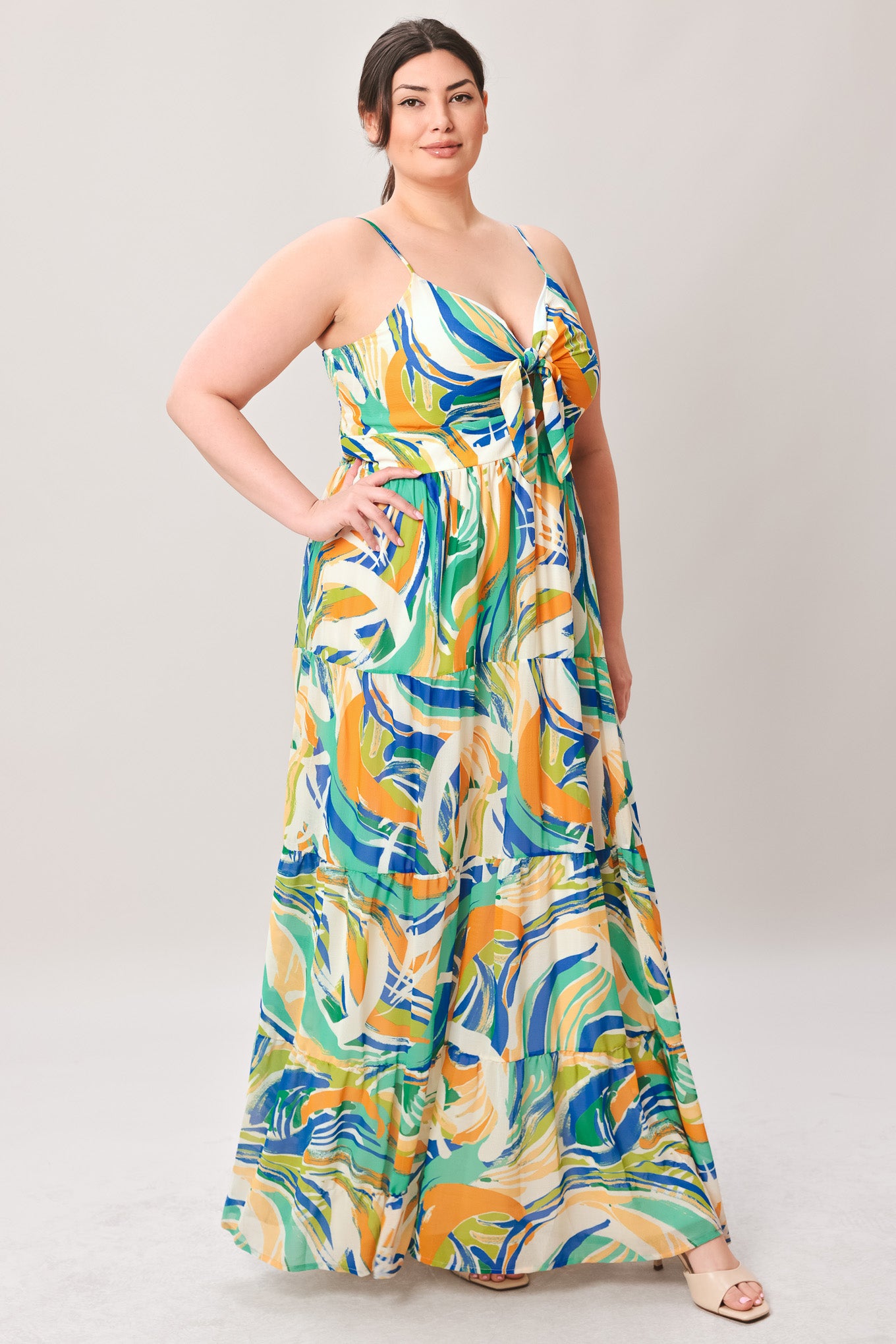 Woman wearing a colorful patterned maxi dress featuring cami bodice with front tie and cut out detail, tiered skirt and smocked back bodice on a plain background | Curve | Flying Tomato