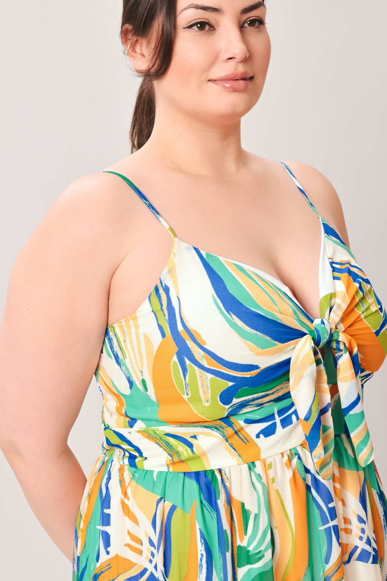 Woman wearing a colorful patterned maxi dress featuring cami bodice with front tie and cut out detail, tiered skirt and smocked back bodice on a plain background | Curve | Flying Tomato