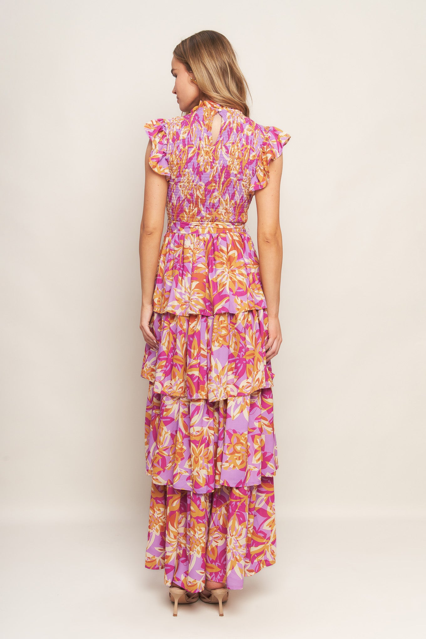 A printed woven midi dress featuring ruffled neckline, sleeveless with ruffled edge, smocked bodice, self belt, layered skirt and back neck button closure