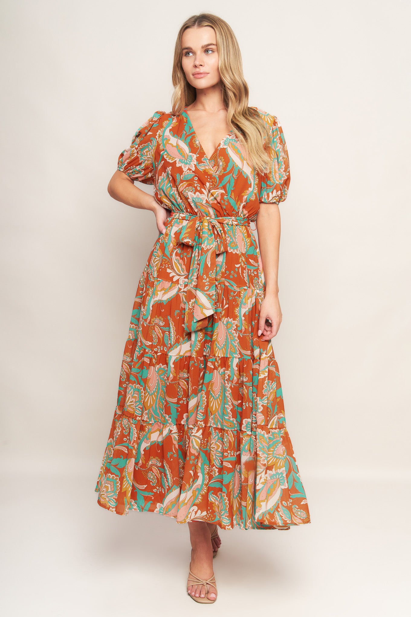 A printed woven midi dress featuring surplice neckline, short sleeve, elasticized waist with self sash tie and tiered skirt