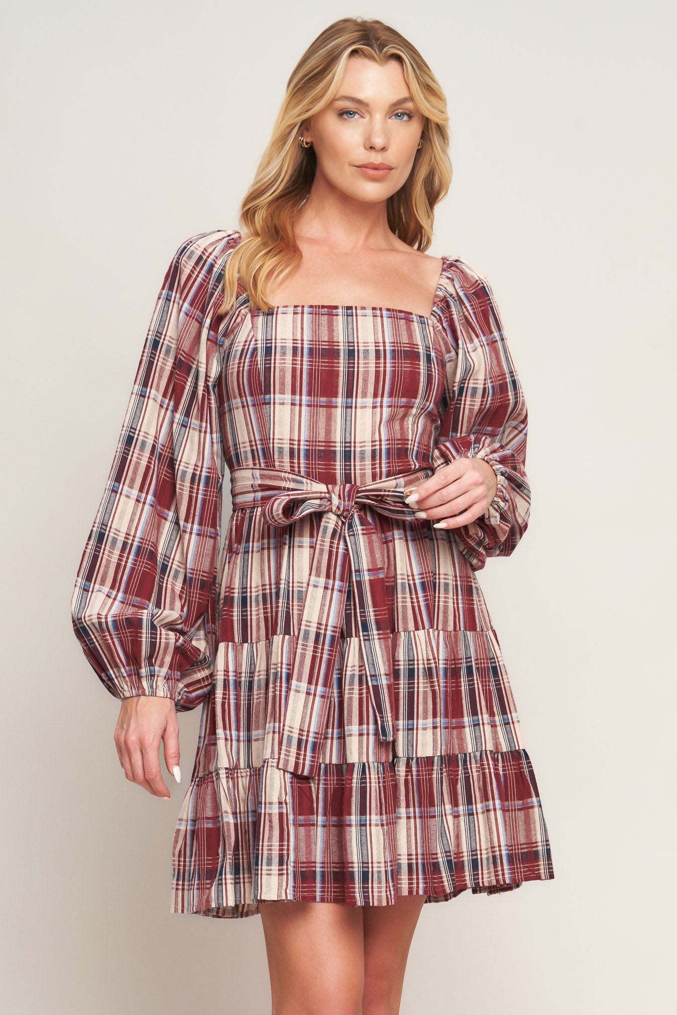 A woven plaid mini dress featuring square neckline, long sleeve, self sash tie, tiered skirt and smocked back bodice