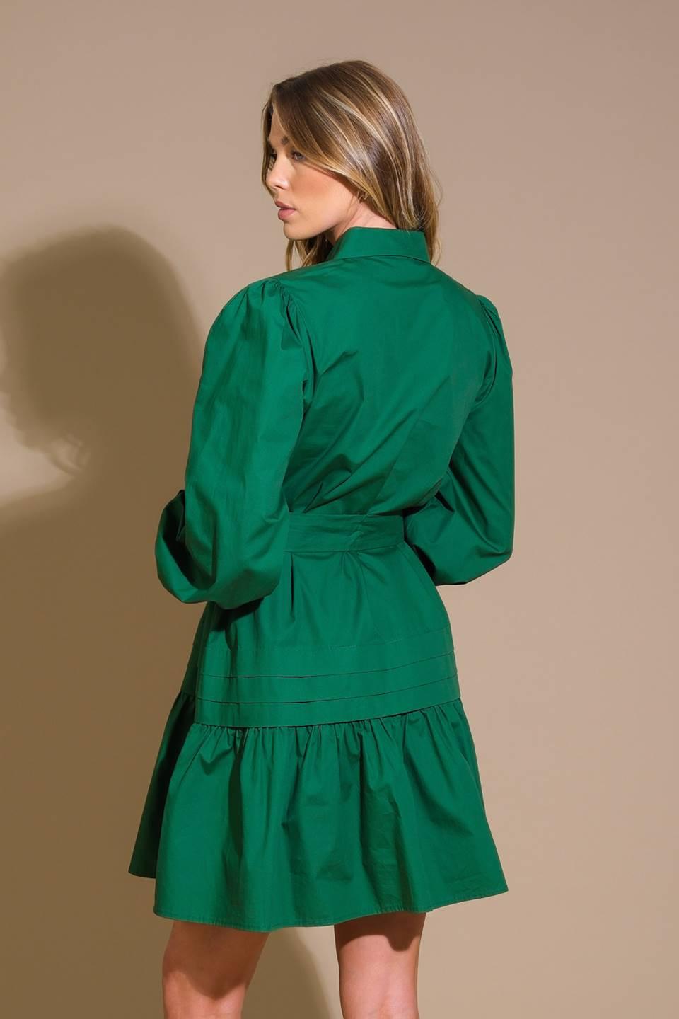 A solid woven mini dress featuring a shirt collar, button down, front pleats, long sleeve, self-sash tie, and ruffled hemline