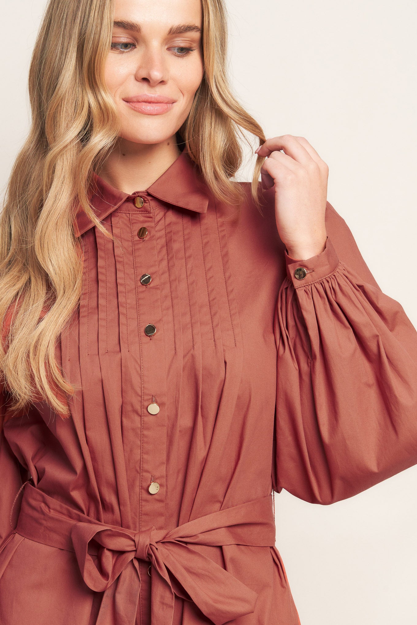 A solid woven mini dress featuring a shirt collar, button down, front pleats, long sleeve, self-sash tie, and ruffled hemline