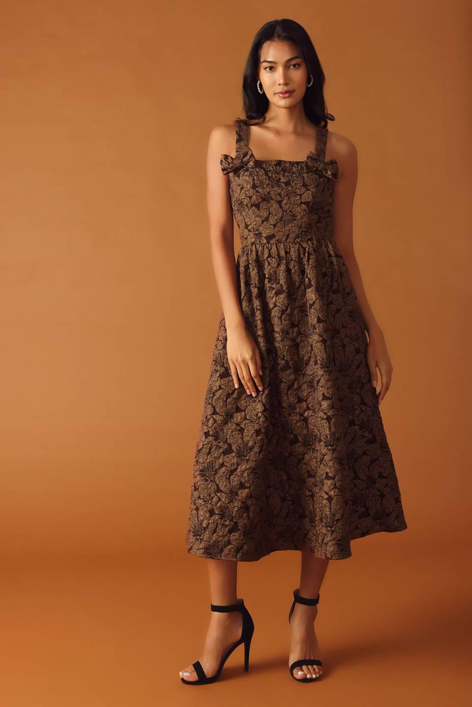 A brown textured woven midi dress featuring straight neckline, strap with bow, full skirt with back zipper closure on a white background | Flying Tomato