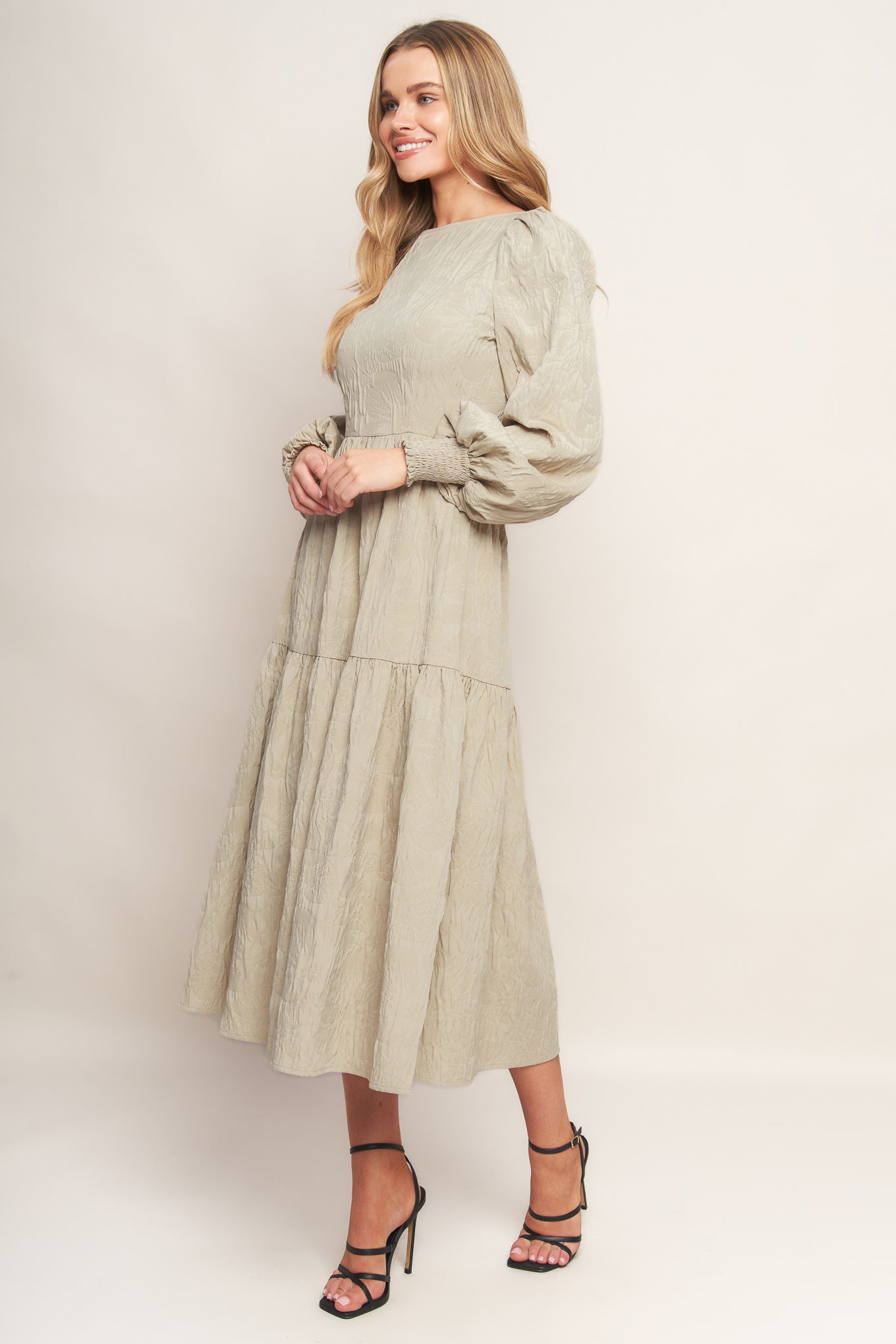 A textured woven midi dress featuring wide neckline, long sleeve with smocked cuff, tiered skirt and back zipper closure