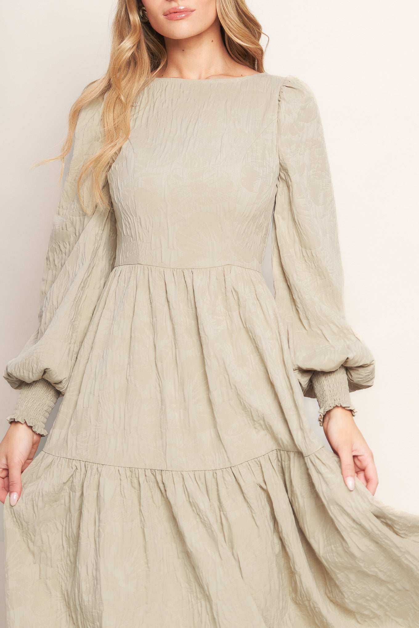 A textured woven midi dress featuring wide neckline, long sleeve with smocked cuff, tiered skirt and back zipper closure
