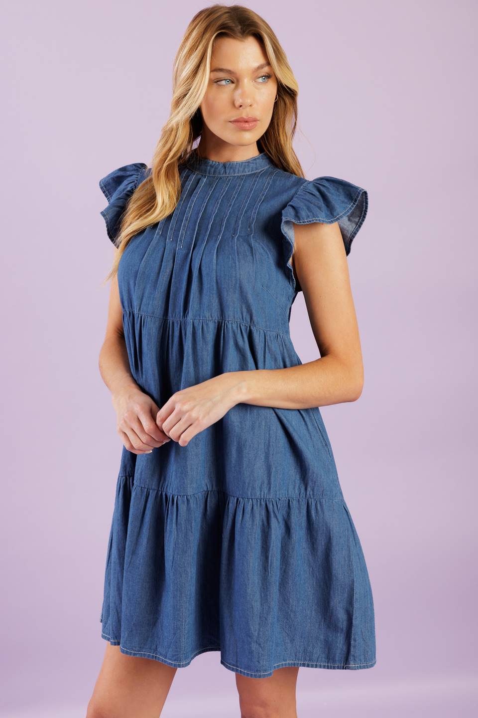 A woven chambray mini dress featuring round neckline, short ruffled sleeve, front pin tuck bodice, tiered body and back button closure.