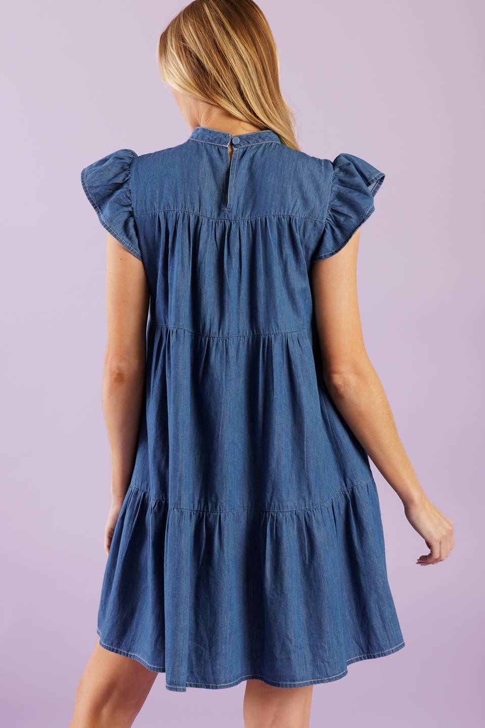 A woven chambray mini dress featuring round neckline, short ruffled sleeve, front pin tuck bodice, tiered body and back button closure.