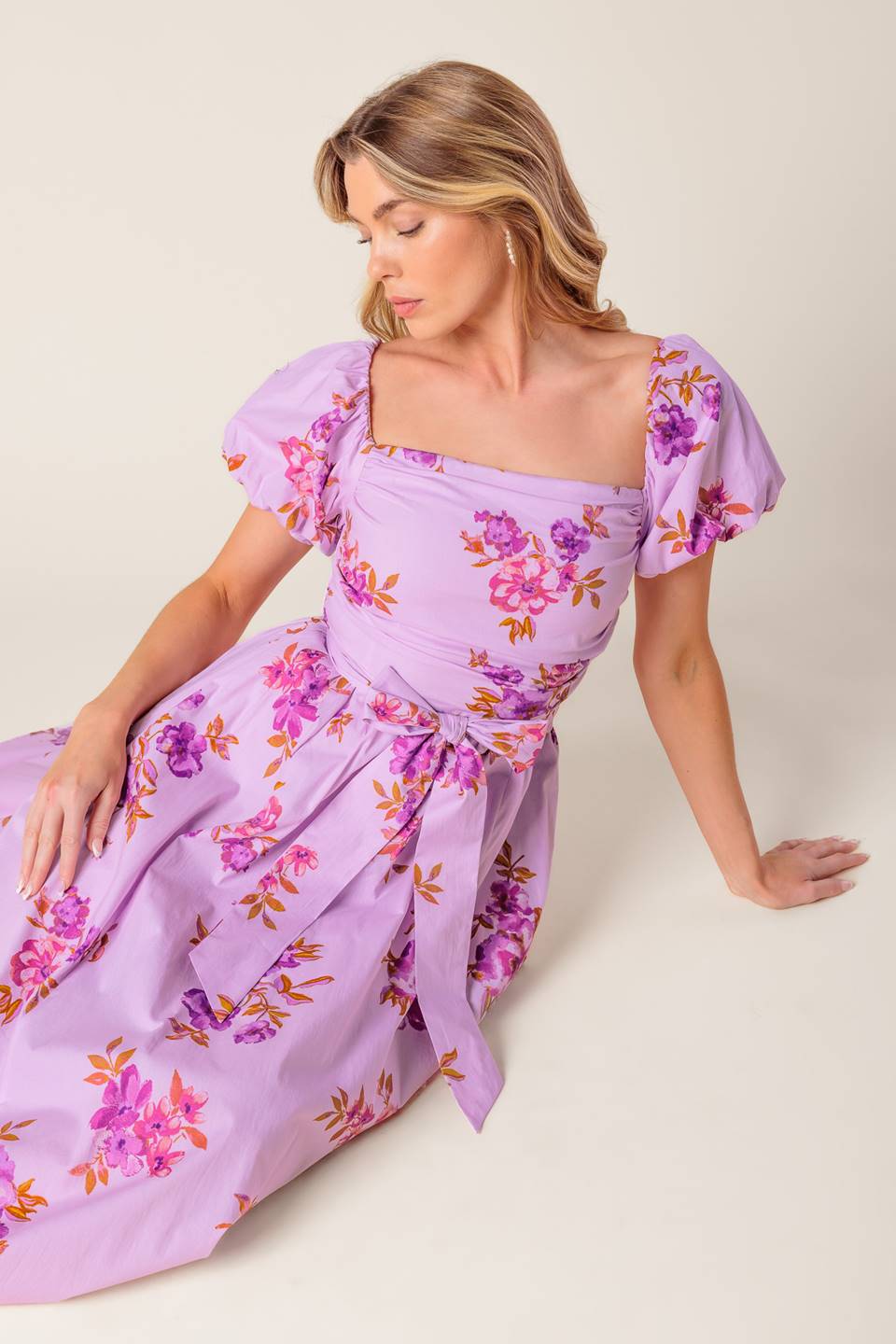 A lavender printed woven midi dress featuring on/off shoulder neckline, shirred bodice, self sash tie, full skirt and smocked back bodice.